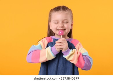 Happy little girl with lollipop on orange background