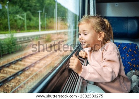 Happy little girl looking out train window outside, while it moving. Traveling by railway, Europe. High quality photo