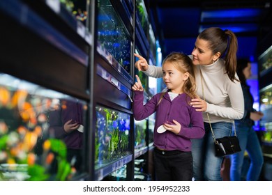 Happy Little Girl With Mother Choosing New Aquarium Fish For Home Fish Tank In Pet Store