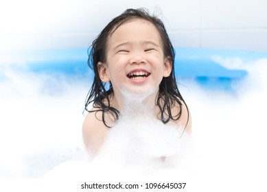 Happy Little Girl Playing In Bath Tube With Foam Bubbles. Little Child In A Bathtub, Smiling Kid In Bathroom, Hygiene And Care For Young Children.