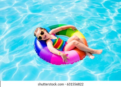 Happy Little Girl Playing With Colorful Inflatable Ring In Outdoor Swimming Pool On Hot Summer Day. Kids Learn To Swim. Child Water Toys. Children Play In Tropical Resort. Family Beach Vacation.