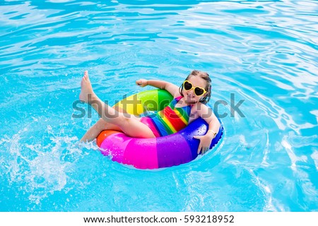 Happy little girl playing with colorful inflatable ring in outdoor swimming pool on hot summer day. Kids learn to swim. Child water toys. Children play in tropical resort. Family beach vacation.