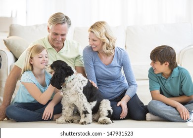 Happy Little Girl Playing With Dog While Family Looking At Her In Living Room