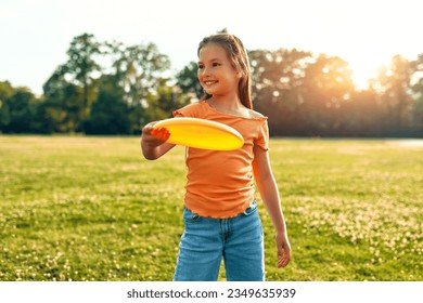 Happy little girl playing frisbee in a meadow in the park, having fun on a warm sunny day off.