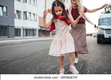 A Happy Little Girl Playing Hopscotch With Her Mother On A Playground Outside. A Child Plays With Her Mom. Kid Plays With Mum Hopscotch Drawn On The Pavement. Activities And Games For Children.