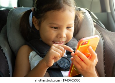 A Happy Little Girl Playing And Watching Tv On A Cell Phone Sitting In A Car Seat. Kids Using Electronics.