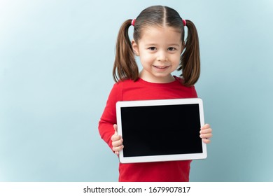Happy little girl with ponytails showing the screen of a tablet computer and smiling in a studio