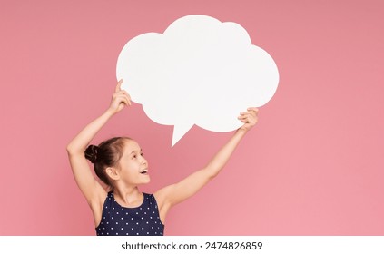 Happy little girl with raised hands holding blank speech bubble, pink studio background - Powered by Shutterstock