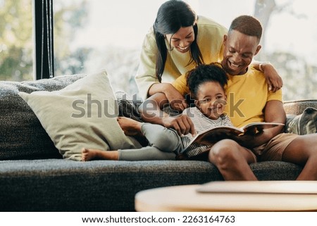 Happy little girl reading a story with her mother and father. Parents giving their child attention at home. Fun family moments on the weekend.