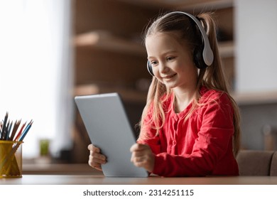 Happy little girl resting at home with digital tablet, cute preteen female child wearing wireless headphones playing online game, happy kid watching videos on modern gadget, copy space - Powered by Shutterstock