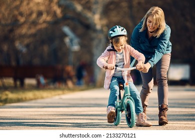 Happy Little Girl Riding Bicycle With Mother's Assistance In The Park. Copy Space.