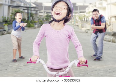 Happy little girl riding bicycle with her dad and brother clapping hands at the back - Powered by Shutterstock