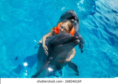 Happy Little Girl Riding the Dolphin in Swimming Pool