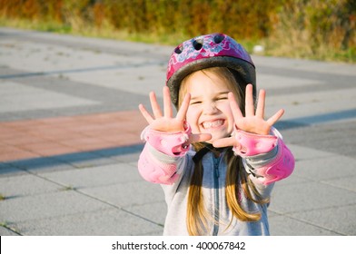 happy little girl roller skating wearing protection and pink helmet waving