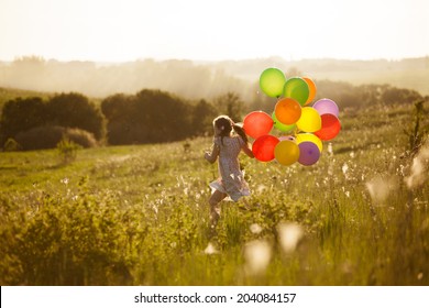 Happy little girl running across the field with balloons