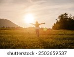 Happy little girl running on background mountains and sky during amazing summer sunset. Child runs with arms raised like wings of an airplane, childhood dream holiday. Kid dream, airplane pilot