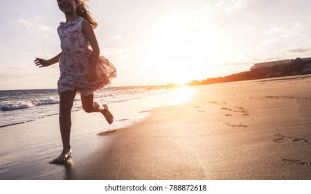 Happy Little Girl Running On The Beach At Sunset - Kid Having Fun In Holiday Vacation With Back Sun Light - Youth, Lifestyle And Happiness Concept - Focus On Silhouette