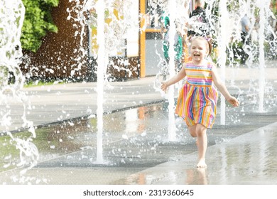 A happy little girl runs near the fountain and looks joyfully ahead. The child has a rest near a fountain during a heat wave.