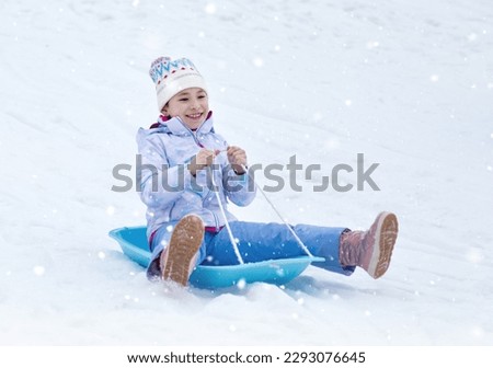 Happy little girl slides down a hill on a sled. 