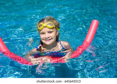 Happy Little Girl Swimming With A Pink Foam Noodle In A Pool 