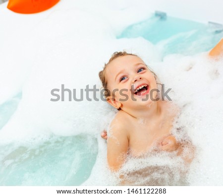 Happy little girl takes a bath in a hydromassage bathtub with foam.