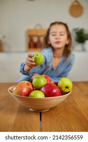 Happy little girl takes a pear from the bowl with variety fruits on table at home, child eating healthy snack, vegetarian nutrition for kids, vitamins for children.
