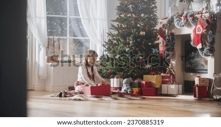 Happy Little Girl Waking Up on Holiday Morning to Receive New Toys from Under the Christmas Tree. Cute Child Getting Her Gift from Santa