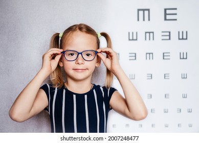 Happy Little Girl Wearing Glasses Taking Eyesight Test Before School With Blurry Eye Chart At The Background, Child's Vision Examination