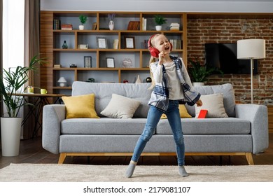 Happy Little Girl Wearing Red Headphones Dancing And Singing, Jumping On A Floor. Cute Child Enjoy Listening Favorite Music Tracks In Mobile Application. Home Leisure, Happy Childhood