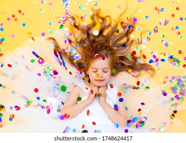 Happy little girl in a white dress celebrates a party with confetti top view. Birthday child, positive emotions.