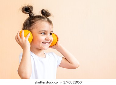 happy little girl in a white t-shirt holds two orange oranges in her hands - Shutterstock ID 1748331950