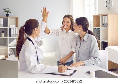 Happy little girl who visits doctor with her mother gives high five to female doctor at hospital meeting. Smiling teen girl celebrating successful treatment finish with general practitioner at checkup
