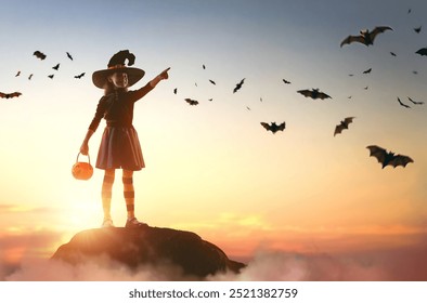 Happy little girl in witch costume at Halloween. Kid on sunset sky background.