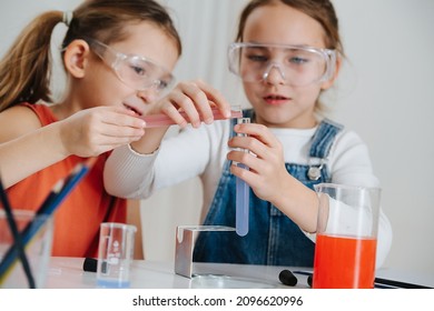 Happy little girls doing science project, they are mixing two colored liquids, pouring from one flask into another. Both wearing protective glasses. - Powered by Shutterstock