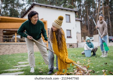 Happy Little Girls With Grandmother And Mother Cleaning Up Garden From Leaves In Autumn