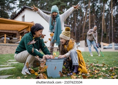 Happy little girls with grandmother picking up leaves and putting them in bucket in garden in autumn - Powered by Shutterstock