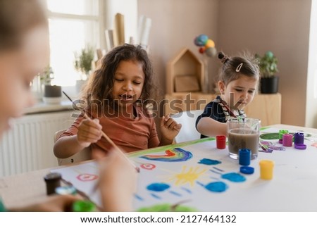 Happy little girls painting picture during creative art and craft class at school.