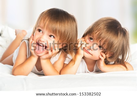 happy little girls twins sister in bed under the blanket having fun, smiling