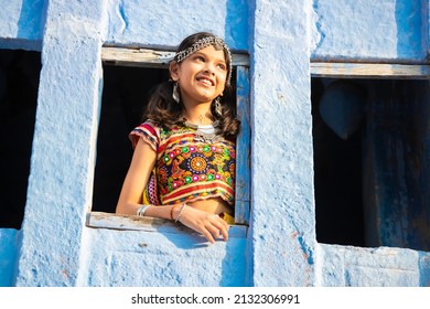 Happy little indian girl kid wearing traditional colorful rajasthani outfit and jewelery looking out of window.