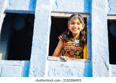 Happy little indian girl kid wearing traditional colorful rajasthani outfit and jewelery looking out of window.