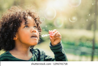 Happy little kid blowing soap bubble in school garden. Child outdoor activity concept. - Powered by Shutterstock