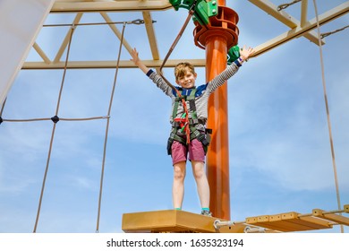 Happy Little Kid Boy Climbing On High Rope Course Trail. Active Child Making Adventure And Action On Family Vacations. Challenge For Brave Kids.