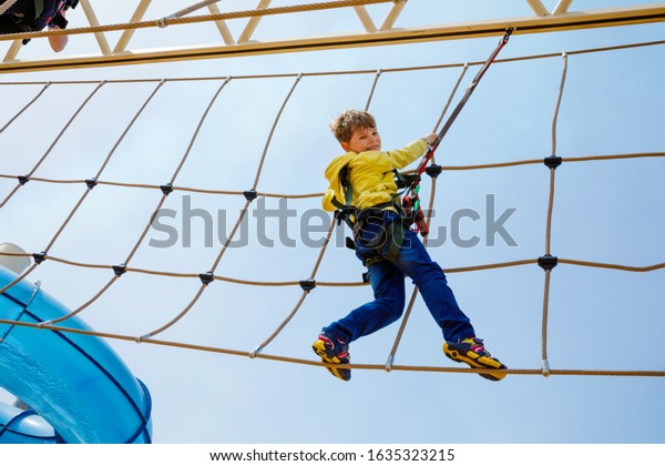 Happy little kid boy climbing on high rope\
course trail. Active child making adventure and action on family\
vacations. Challenge for brave\
kids.