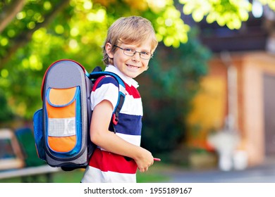 Happy little kid boy with glasses and backpack or satchel on his first day to school or nursery. Child outdoors on warm sunny day, Back to school concept.