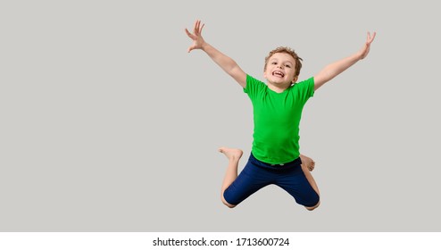 Happy Little Kid Boy In Green T-shirt On Gray Background Is Smiling, Laughing And Jumping. Children Will Save The Planet Concept. Free Space For You Text And Logo