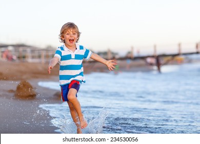 Happy little kid boy having fun with running through water in ocean after sunset