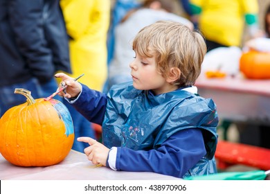 Happy little kid boy on a harvest festival, painting with colors a pumpkin. Child celebrating traditional festival halloween or thanksgiving.