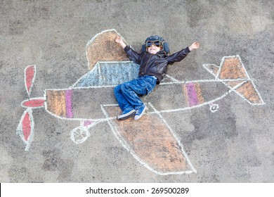 Happy little kid boy in pilot uniform having fun and airplane picture drawing and colorful chalk  Creative leisure for children outdoors in summer 