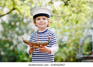 Happy little kid boy in sailor capitain hat and uniform playing with sailor boat ship. Smiling preschool child dreaming and having fun. Education, profession, dream concept - Shutterstock ID 2140102967