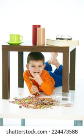 Happy Little Kid Eating Sweets Under Table At Home. Lying On Belly, Happy, Smiling, Isolated On White